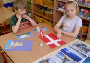 Dzieci siedzące przy stoliku z flagą Danii i obrazkami związanymi z Danią.